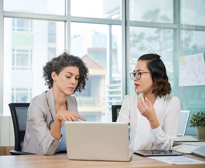 two women talking with a laptop open