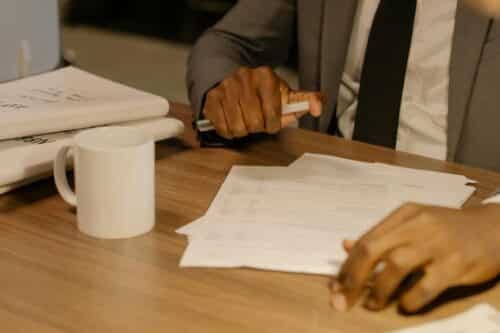 Free Close-up of a businessman holding and reviewing documents on a wooden desk. Stock Photo