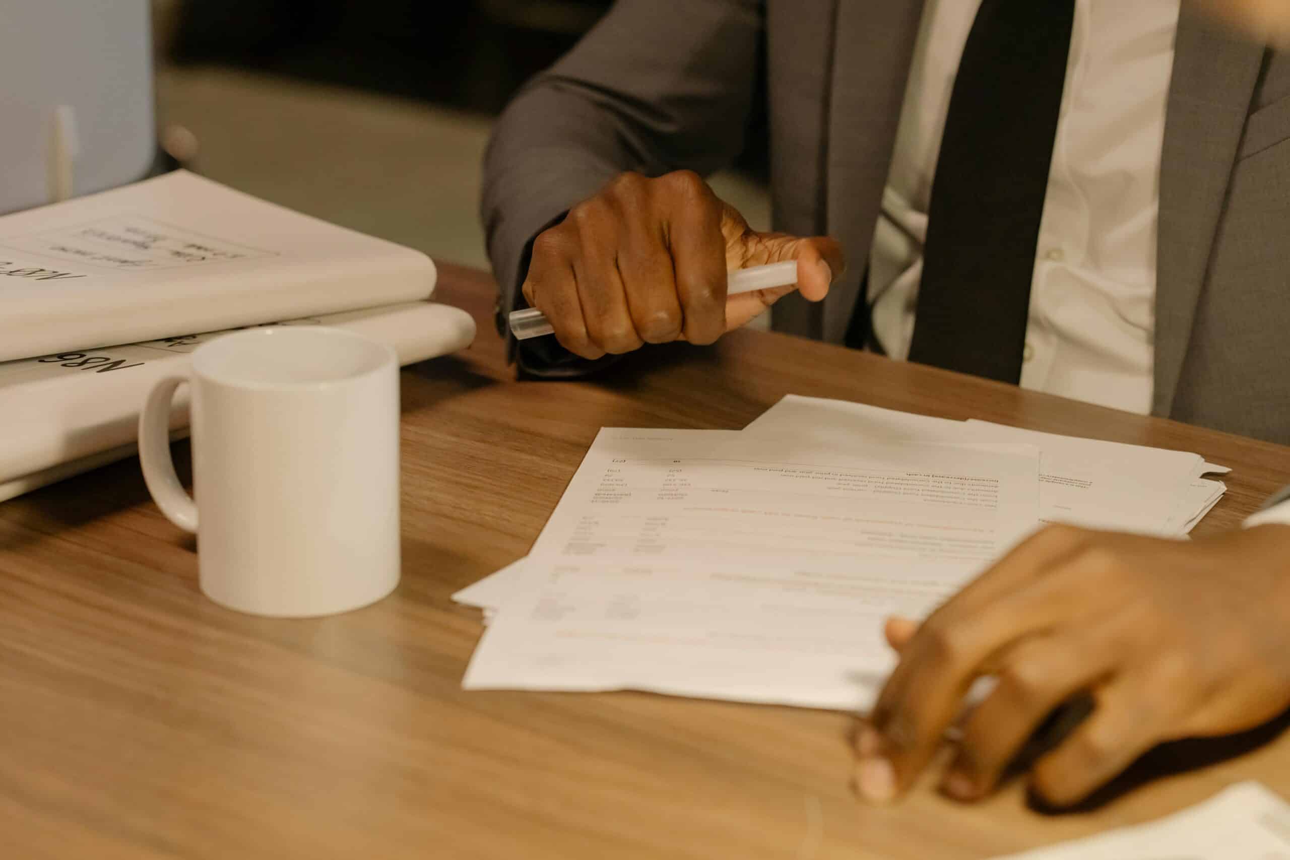 Blog 8 Free Close-up of a businessman holding and reviewing documents on a wooden desk. Stock Photo